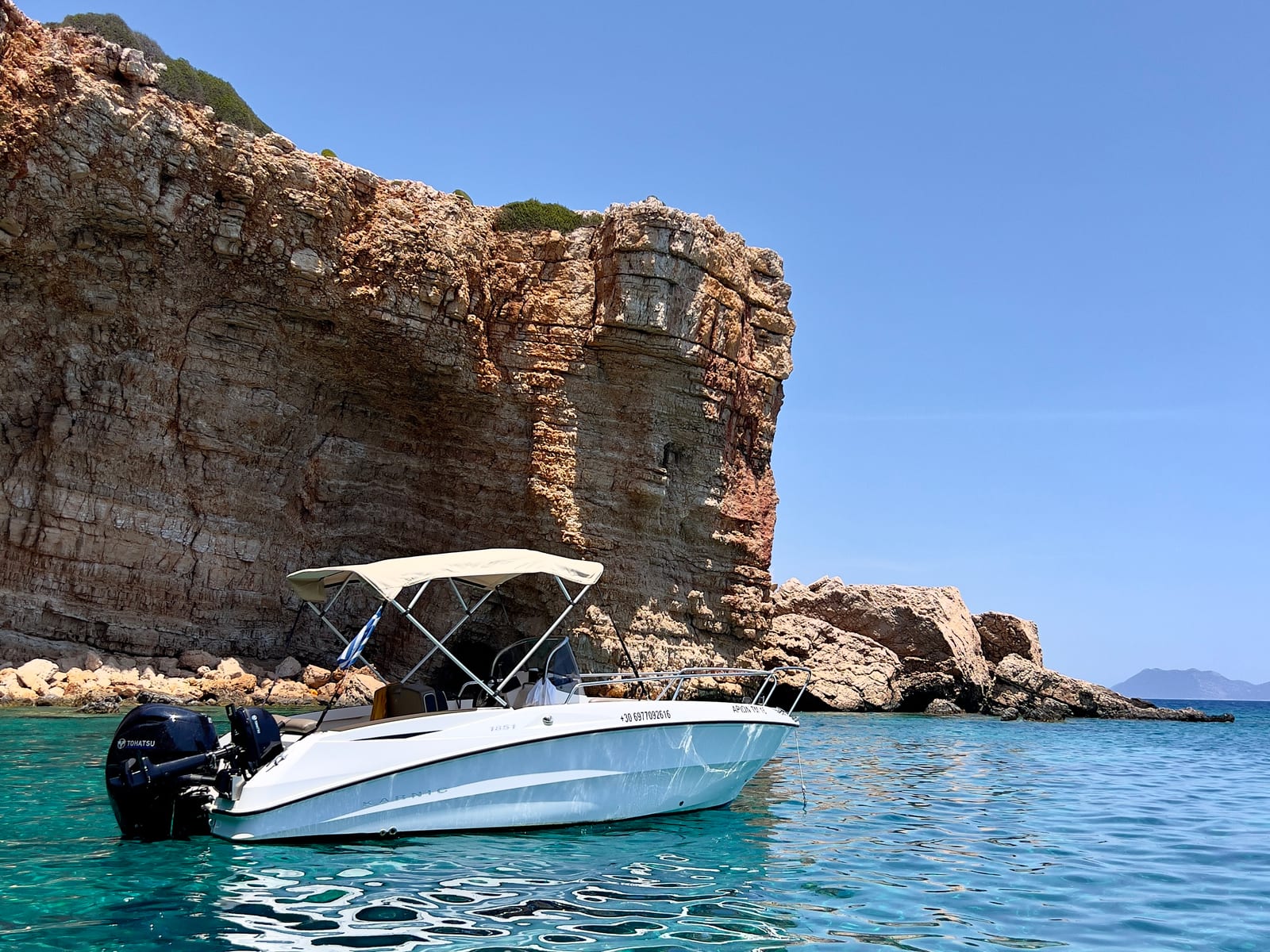 Αρίων anchored beneath the cliffs in clear turquoise water